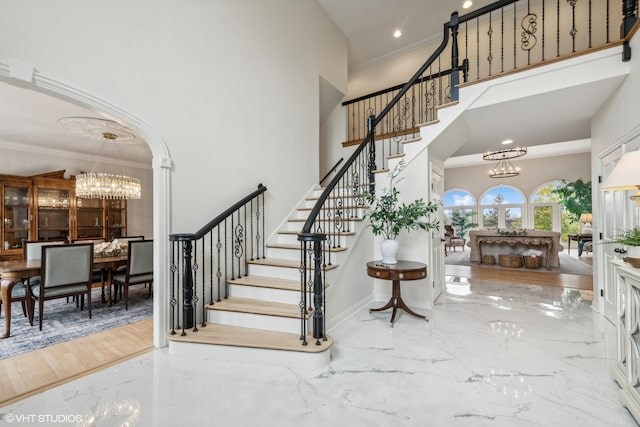 stairs with crown molding, hardwood / wood-style floors, a high ceiling, and an inviting chandelier