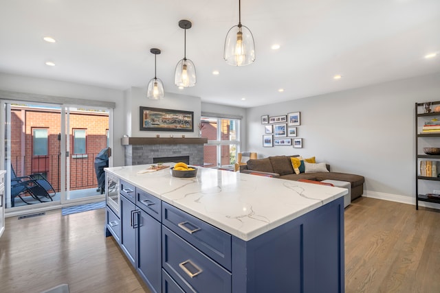 kitchen with dark hardwood / wood-style flooring, a center island, blue cabinetry, pendant lighting, and a fireplace