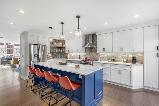 kitchen with white cabinetry, appliances with stainless steel finishes, wall chimney range hood, and a kitchen island