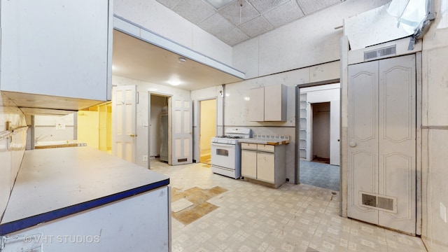 kitchen with white cabinets, white gas range, and a drop ceiling