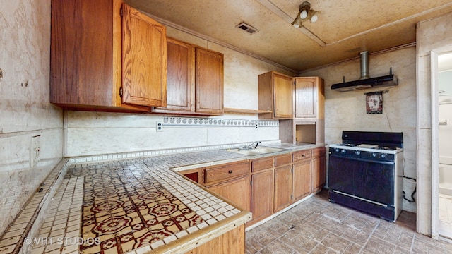 kitchen with tile counters, sink, ornamental molding, extractor fan, and gas range oven