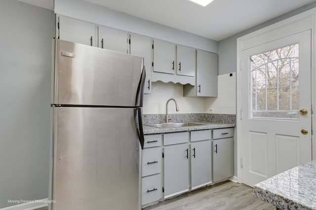 kitchen with backsplash, stainless steel fridge, sink, and light hardwood / wood-style flooring