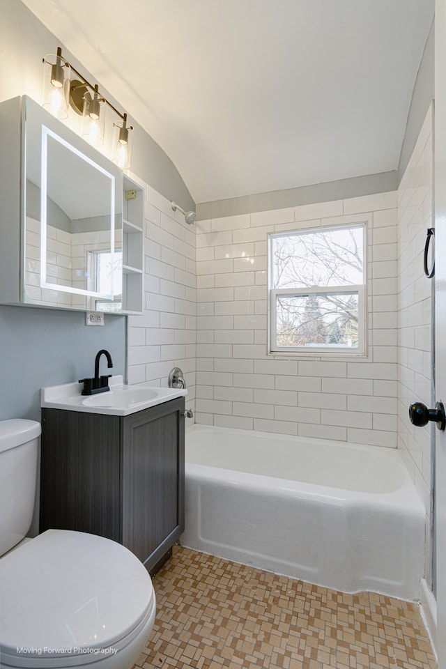 full bathroom featuring toilet, vanity, tiled shower / bath combo, and vaulted ceiling