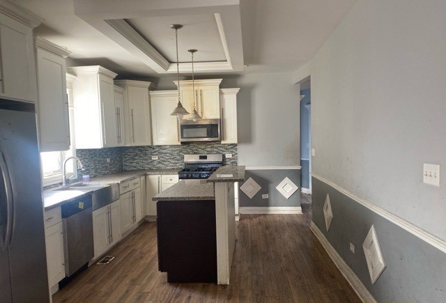 kitchen with stainless steel appliances, decorative light fixtures, dark hardwood / wood-style floors, a tray ceiling, and a center island