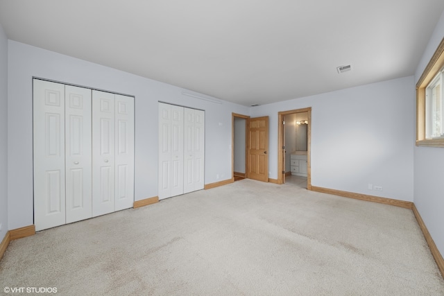 unfurnished bedroom with carpet flooring, ensuite bathroom, and multiple closets