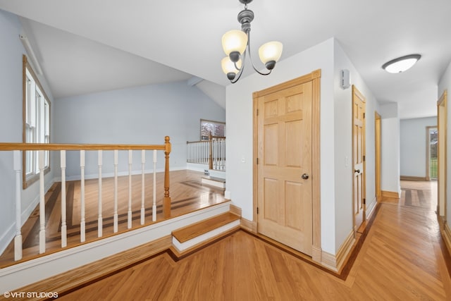 corridor with a chandelier, light hardwood / wood-style floors, and lofted ceiling