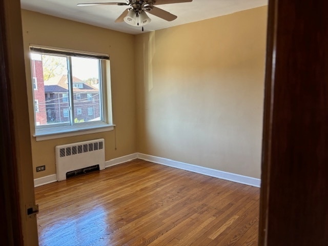 spare room featuring radiator, light wood-type flooring, and ceiling fan