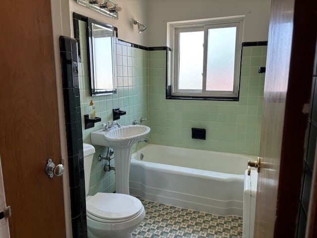 bathroom with toilet, tile walls, and a bathtub