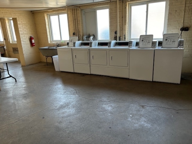 clothes washing area featuring washing machine and dryer and brick wall