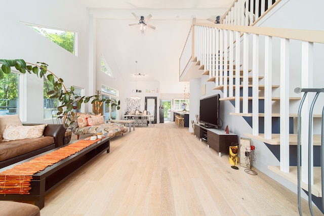 living room with a high ceiling, ceiling fan, a wealth of natural light, and light hardwood / wood-style floors