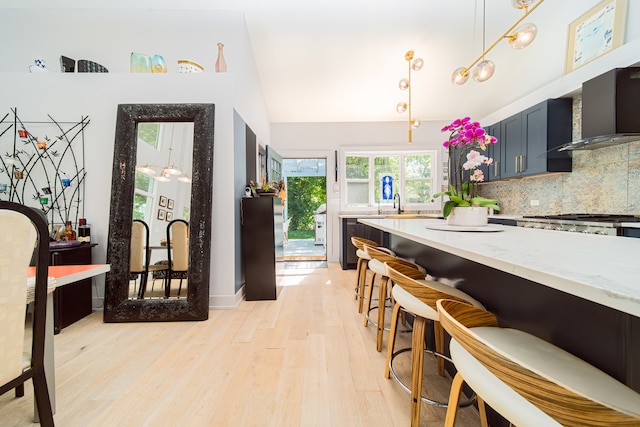 kitchen featuring light stone counters, backsplash, light wood-type flooring, decorative light fixtures, and wall chimney exhaust hood