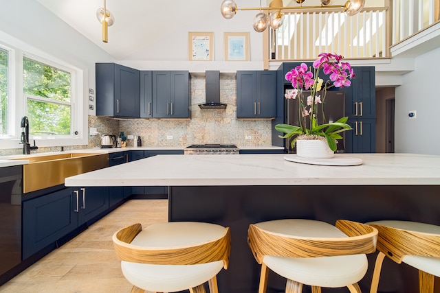 kitchen featuring stainless steel appliances, blue cabinetry, decorative backsplash, a kitchen breakfast bar, and wall chimney exhaust hood