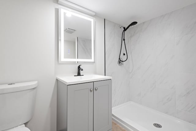 bathroom with a tile shower, vanity, and toilet