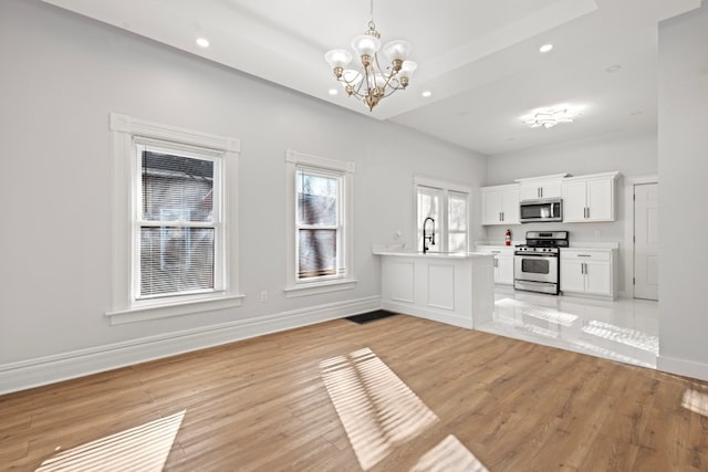 kitchen with white cabinetry, hanging light fixtures, light wood-type flooring, and appliances with stainless steel finishes