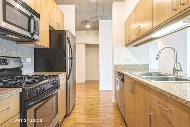 kitchen featuring backsplash, sink, light hardwood / wood-style floors, light stone counters, and stainless steel appliances