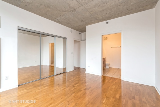 unfurnished bedroom with hardwood / wood-style flooring, ensuite bath, and a closet