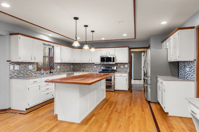 kitchen featuring appliances with stainless steel finishes, white cabinetry, a kitchen island, decorative light fixtures, and light hardwood / wood-style floors