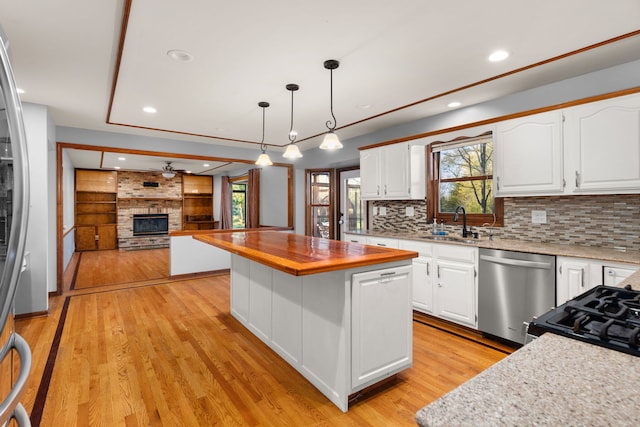 kitchen with appliances with stainless steel finishes, butcher block countertops, decorative light fixtures, a kitchen island, and white cabinetry