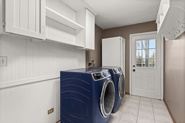 clothes washing area with washing machine and dryer, light tile patterned floors, and cabinets