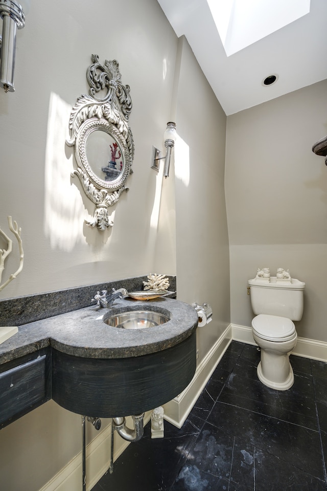 bathroom featuring toilet, vaulted ceiling with skylight, sink, and tile patterned floors