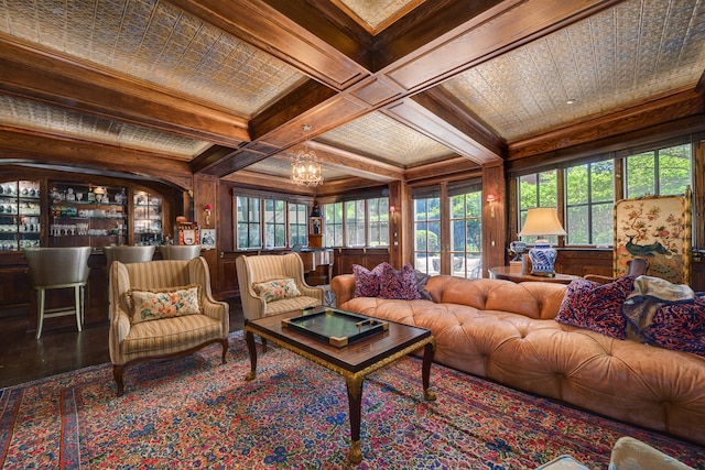 living room featuring wood walls, beamed ceiling, ornamental molding, an inviting chandelier, and coffered ceiling