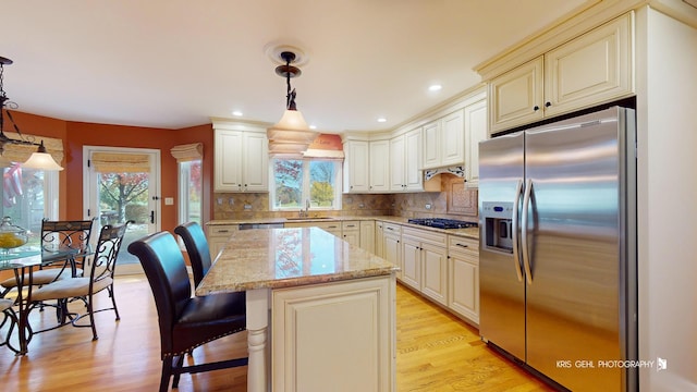 kitchen with appliances with stainless steel finishes, pendant lighting, decorative backsplash, a center island, and light stone countertops