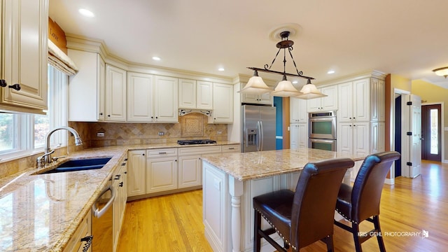 kitchen with sink, light stone counters, hanging light fixtures, a kitchen island, and stainless steel appliances