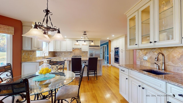 kitchen featuring decorative light fixtures, white cabinetry, sink, light stone counters, and stainless steel appliances