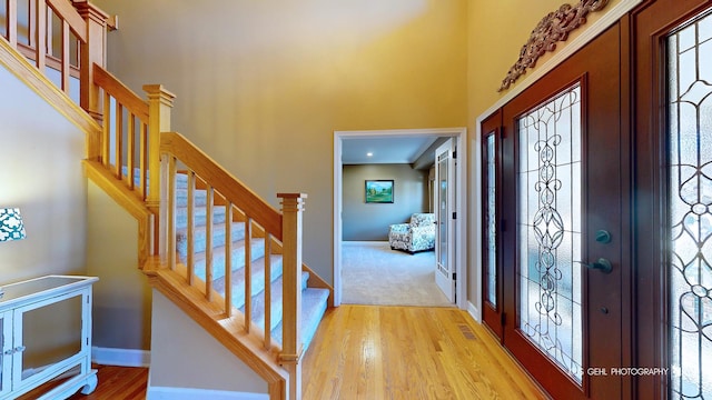 foyer entrance featuring french doors, a towering ceiling, and light hardwood / wood-style flooring