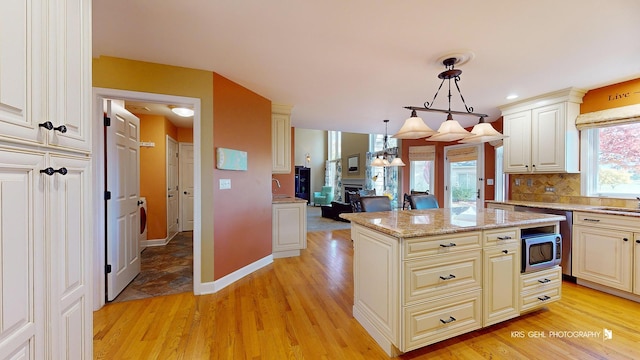 kitchen with hanging light fixtures, a kitchen island, light stone countertops, light hardwood / wood-style floors, and backsplash