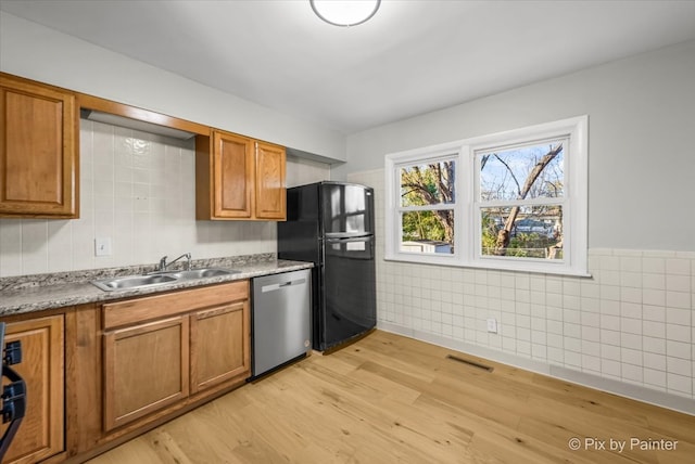 kitchen featuring stainless steel dishwasher, tile walls, sink, and light hardwood / wood-style flooring