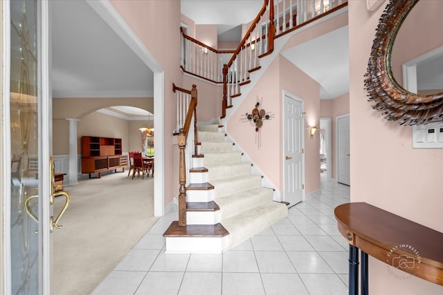 foyer featuring light carpet, a towering ceiling, ornate columns, and crown molding