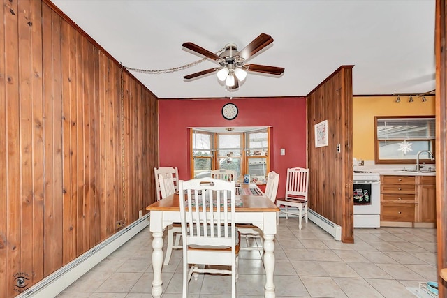 dining area with wooden walls, ceiling fan, a baseboard heating unit, and sink