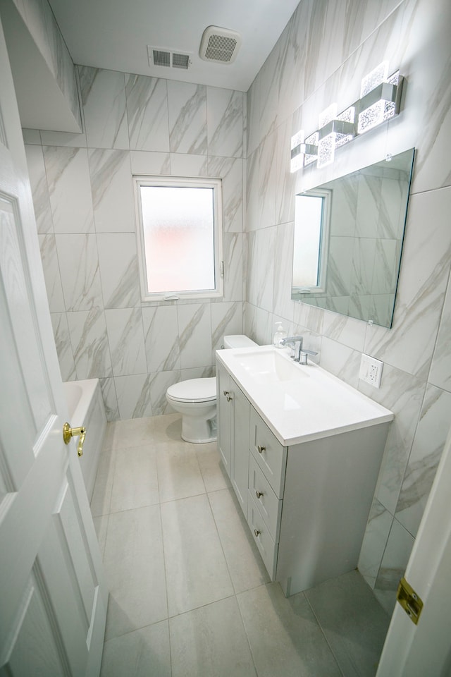 bathroom with tile patterned flooring, vanity, toilet, and tile walls