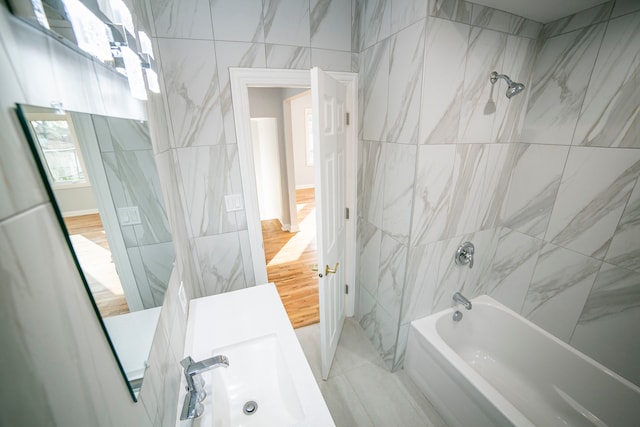 bathroom with wood-type flooring, tile walls, tiled shower / bath, and sink