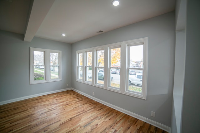 empty room with beamed ceiling, a healthy amount of sunlight, and light wood-type flooring