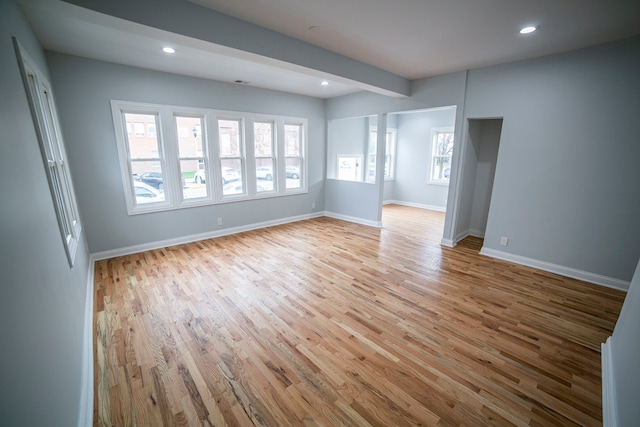 spare room featuring beam ceiling, light hardwood / wood-style floors, and a wealth of natural light