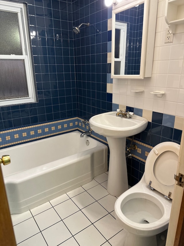 bathroom with tile patterned flooring, tiled shower / bath, toilet, and tile walls