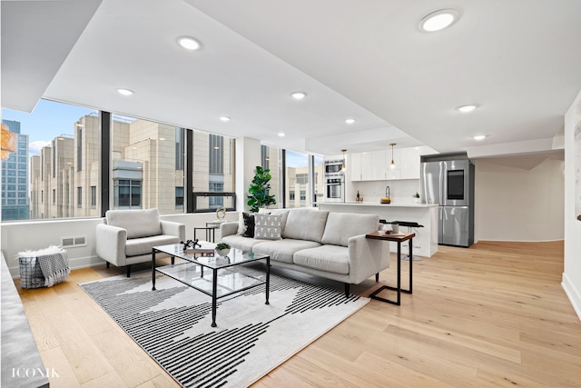 living room featuring visible vents, recessed lighting, a view of city, light wood finished floors, and baseboards