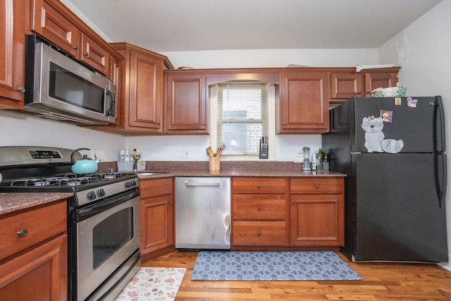 kitchen with appliances with stainless steel finishes, light hardwood / wood-style floors, and dark stone countertops