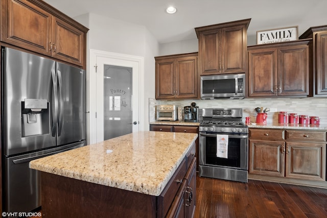 kitchen with a kitchen island, appliances with stainless steel finishes, light stone countertops, decorative backsplash, and dark wood-type flooring