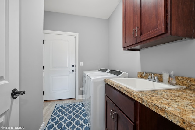 clothes washing area featuring washing machine and dryer, cabinets, sink, and light hardwood / wood-style floors