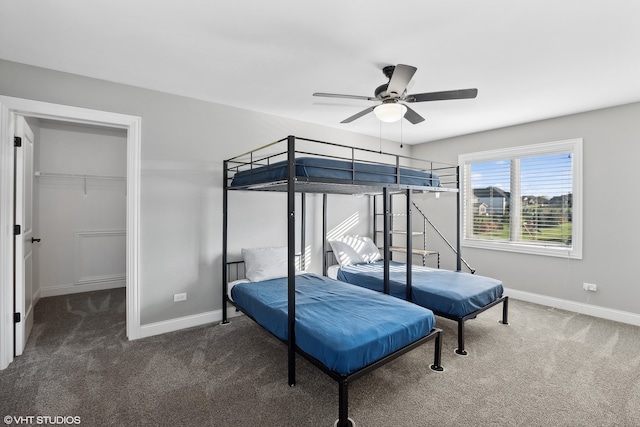 bedroom with a closet, a spacious closet, dark colored carpet, and ceiling fan