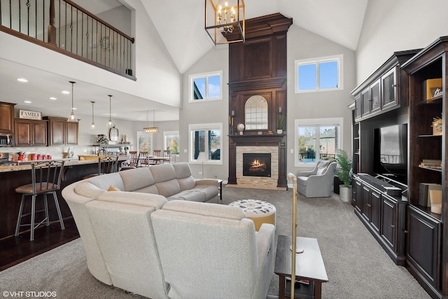 carpeted living room featuring high vaulted ceiling, a fireplace, and a notable chandelier