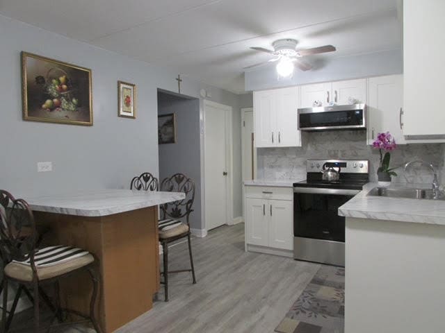 kitchen with sink, a kitchen bar, decorative backsplash, white cabinets, and appliances with stainless steel finishes