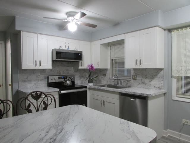 kitchen featuring ceiling fan, sink, stainless steel appliances, backsplash, and white cabinets