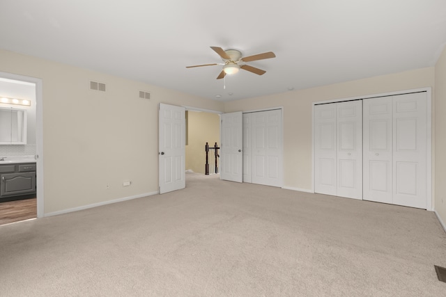 unfurnished bedroom featuring multiple closets, ensuite bath, light carpet, and ceiling fan