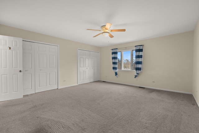 unfurnished bedroom featuring multiple closets, ceiling fan, and carpet