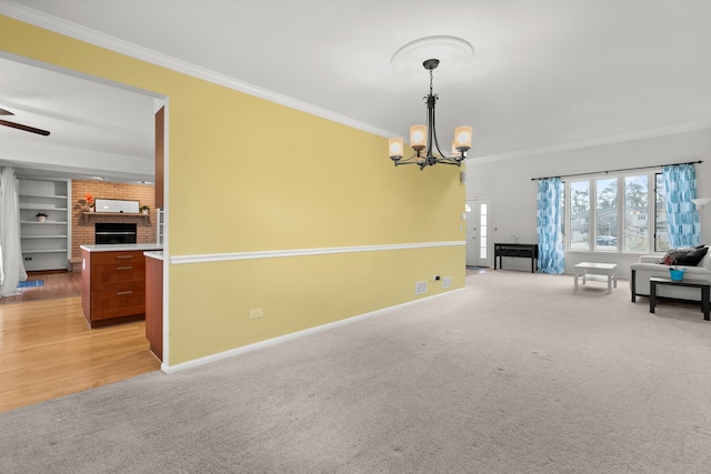 interior space featuring a brick fireplace, ceiling fan with notable chandelier, light colored carpet, built in shelves, and ornamental molding