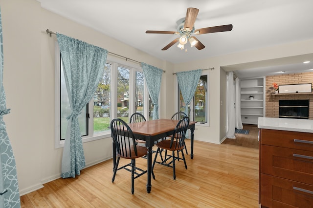 dining space with built in shelves, light wood-type flooring, a fireplace, and ceiling fan